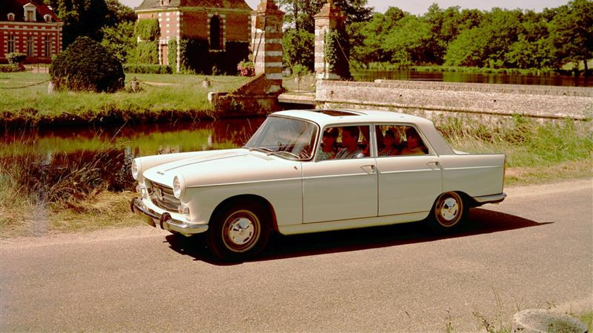 PEUGEOT 404 on a countryside road in front of a red-brick chateau and greenery
